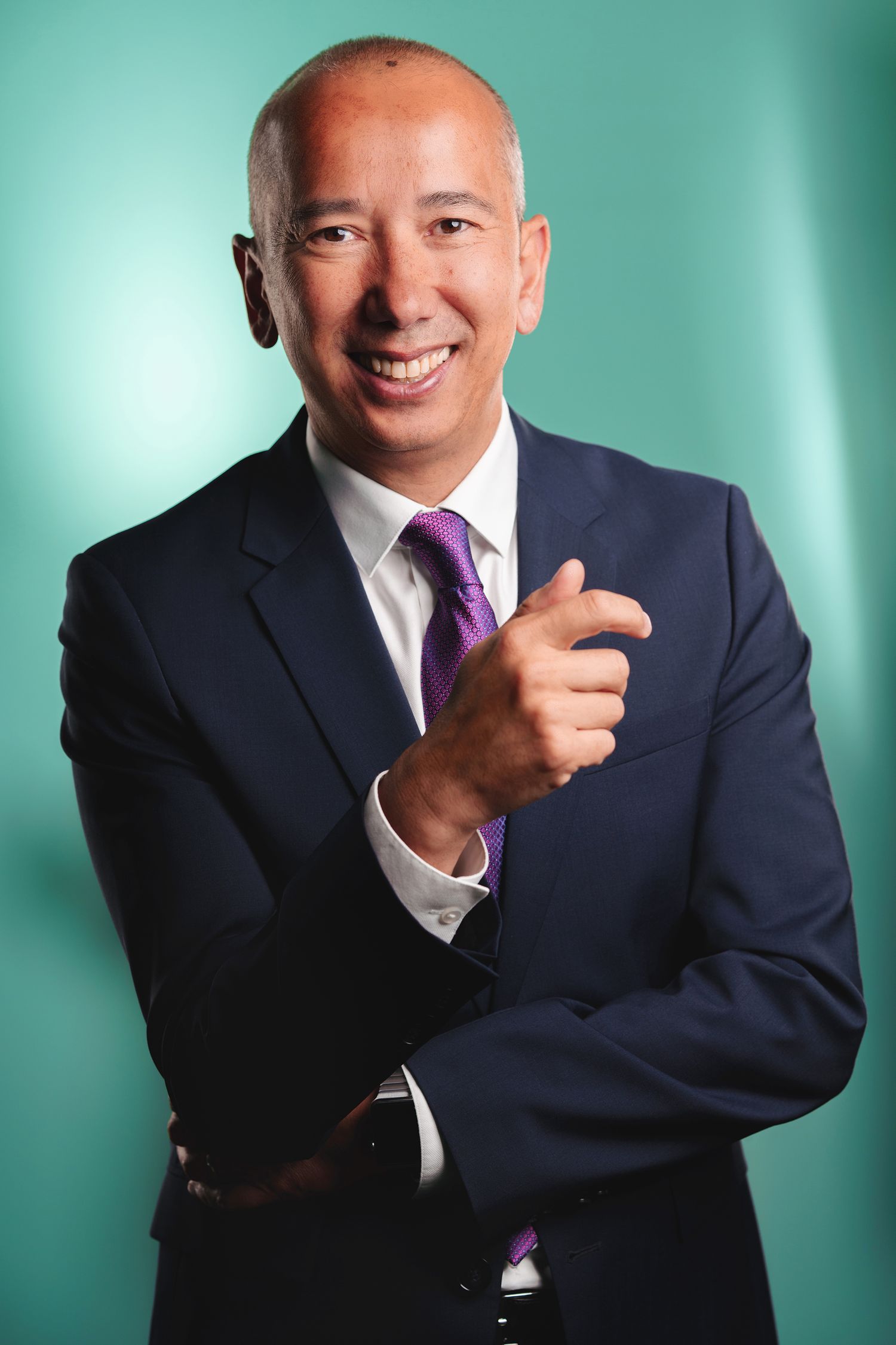 Business professional in navy suit gives thumbs up against teal background.