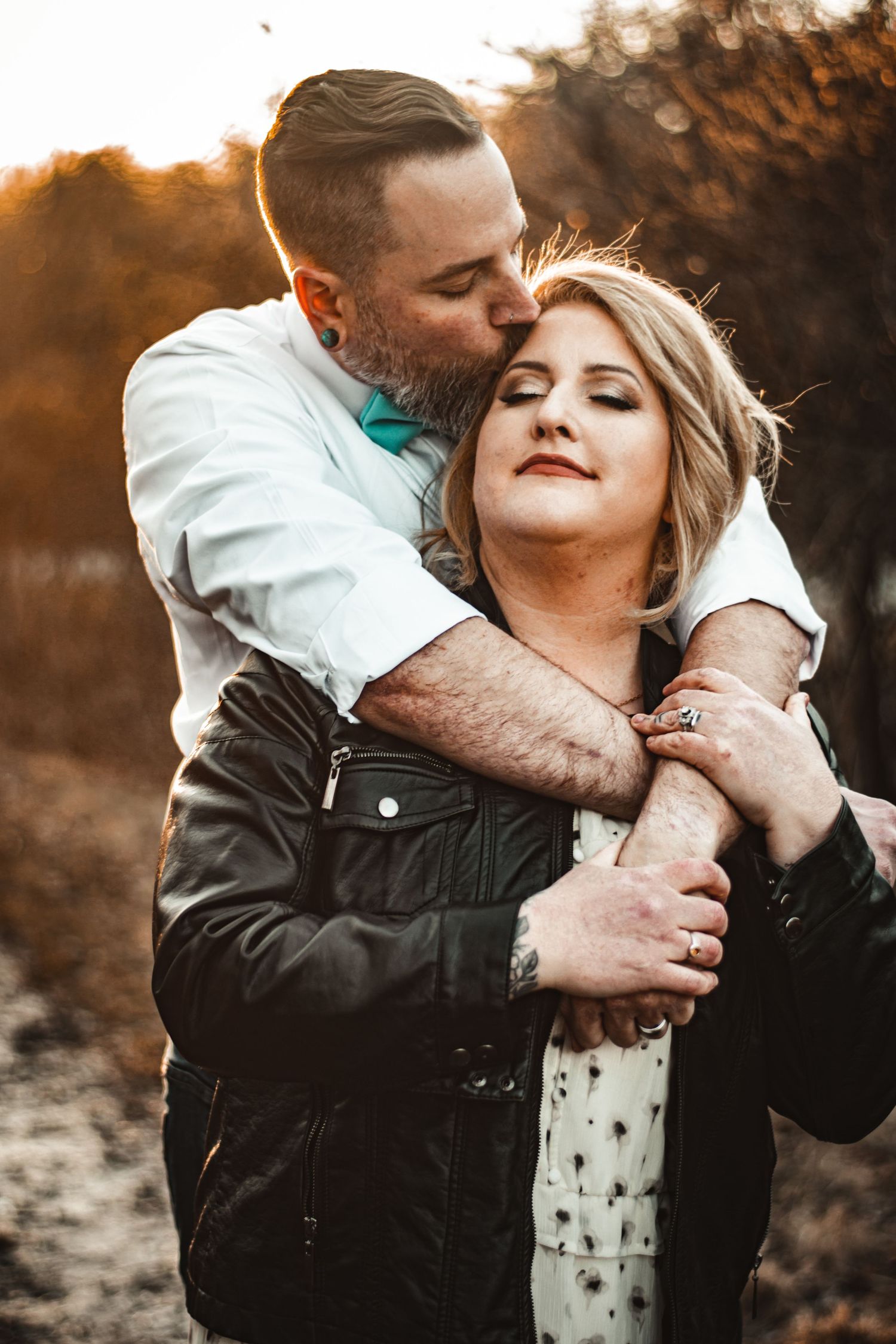 Intimate couple embracing at sunset with warm golden backlight in natural setting.