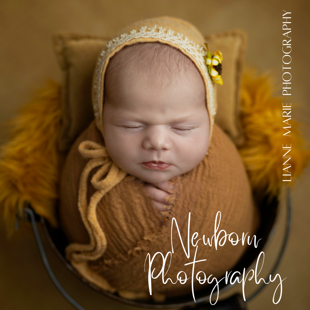 Sleeping newborn wrapped in mustard swaddle on yellow furry backdrop with delicate lace bonnet and floral accent.
