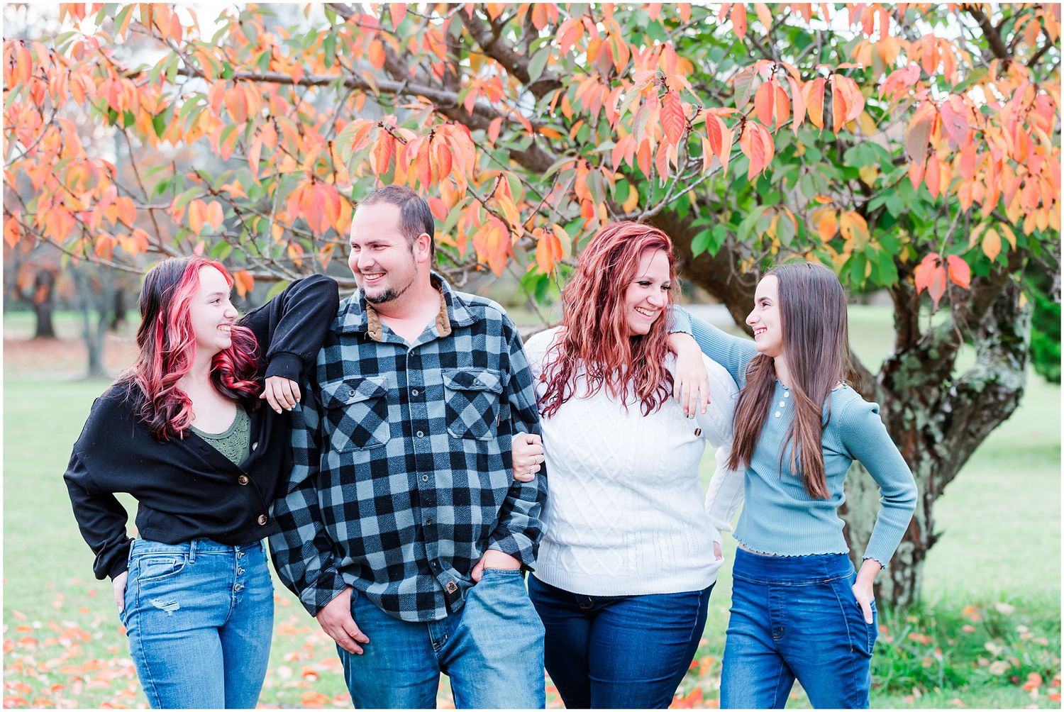 A group of friends laughing together under trees with vibrant coral-colored autumn foliage.