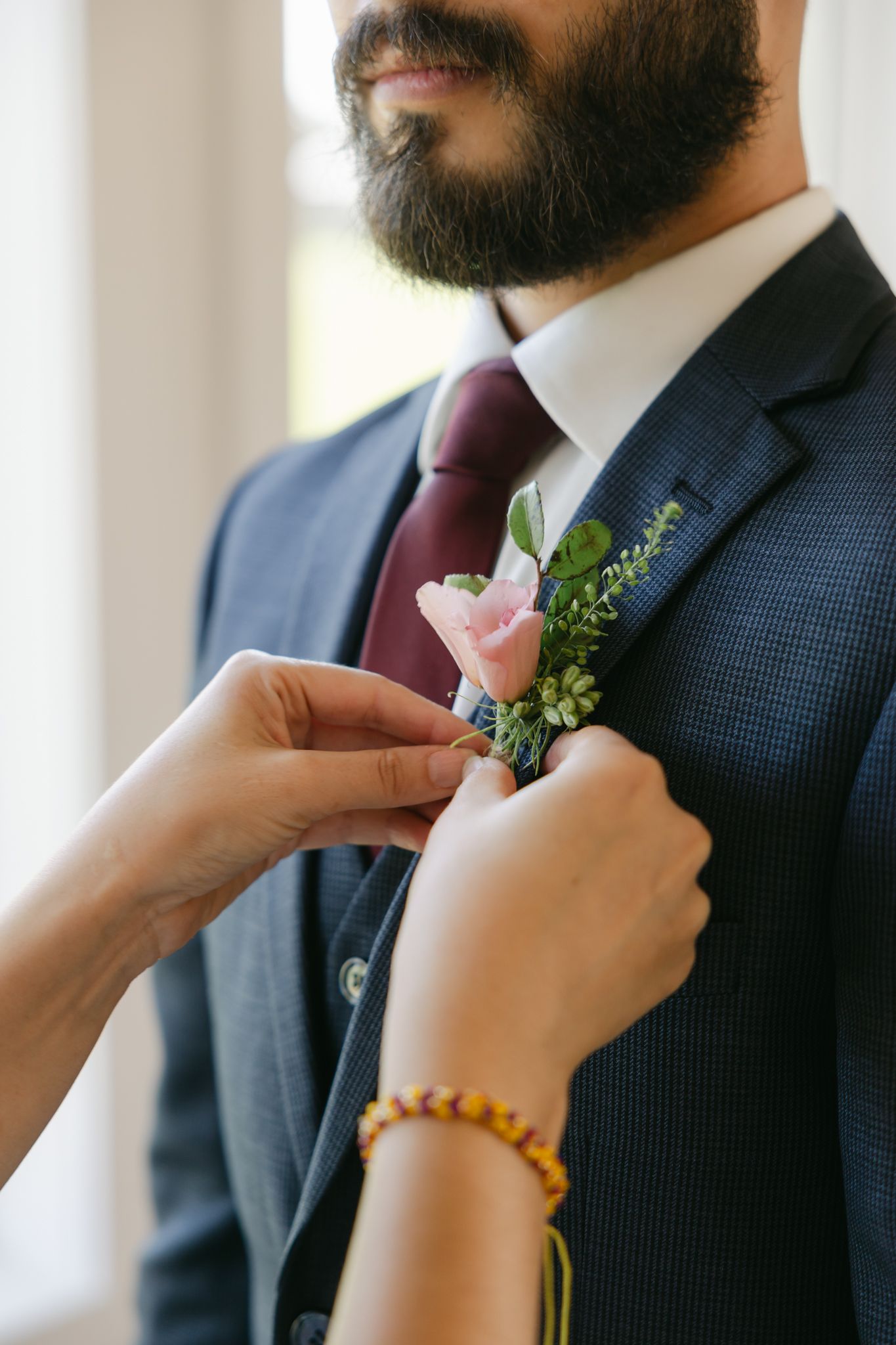 Groom's mom putting his boutonnière on his jacket on wedding day. By Bradenton wedding photographer Popping Champaign