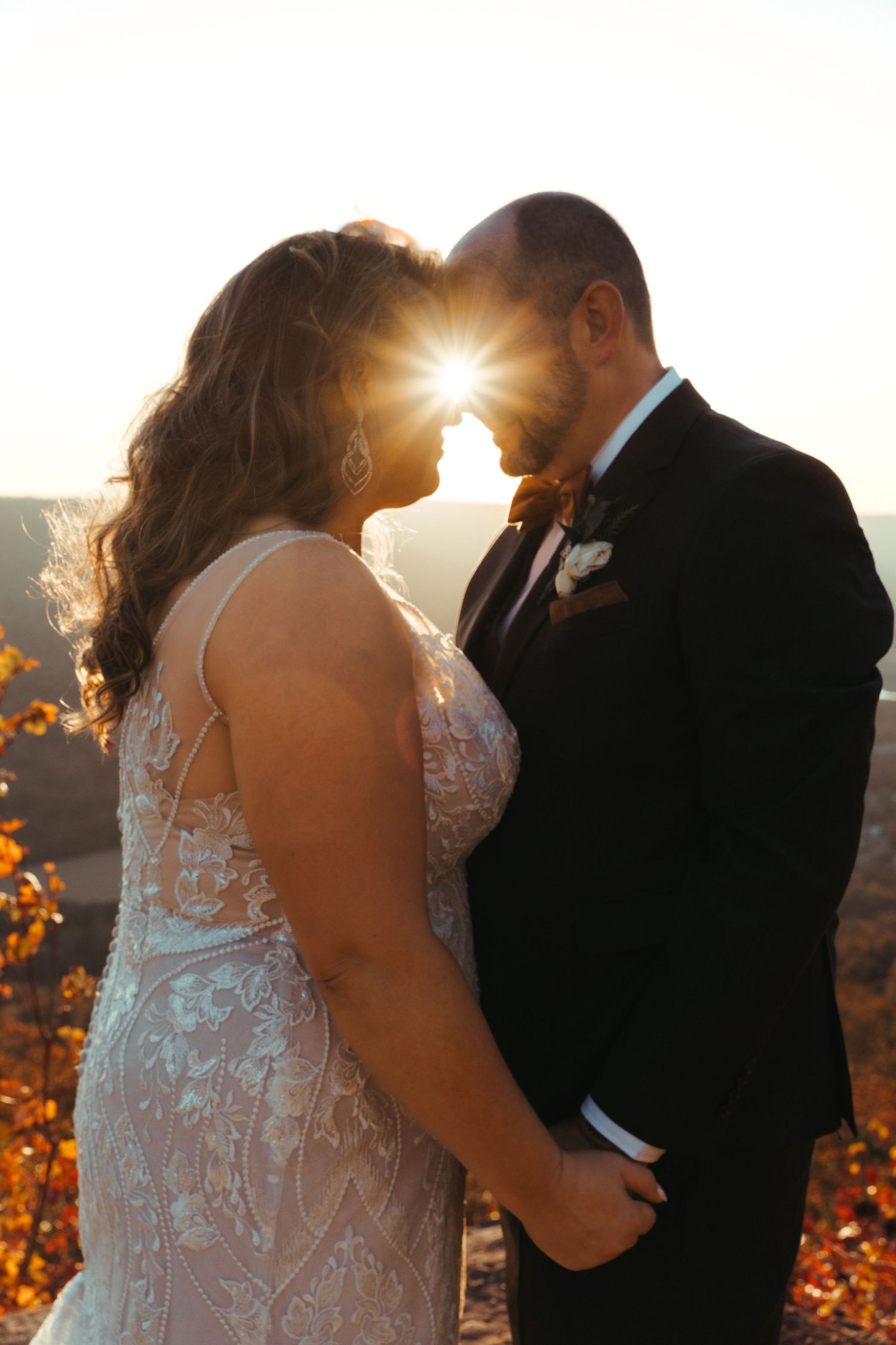 Sunset portrait of newlyweds with sunburst between them in autumn setting.