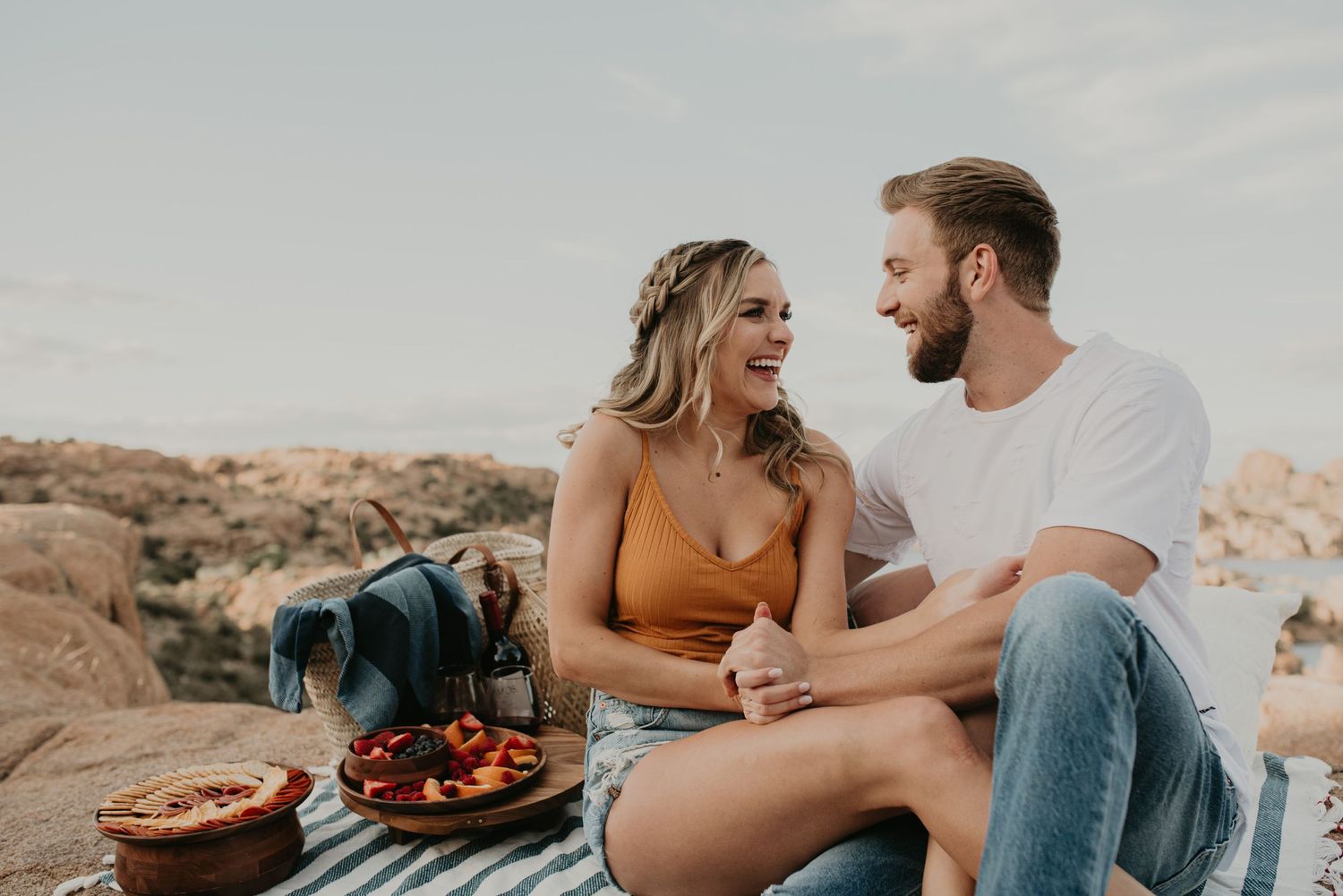 Couple enjoying a picnic on a blanket by the beach at sunset.