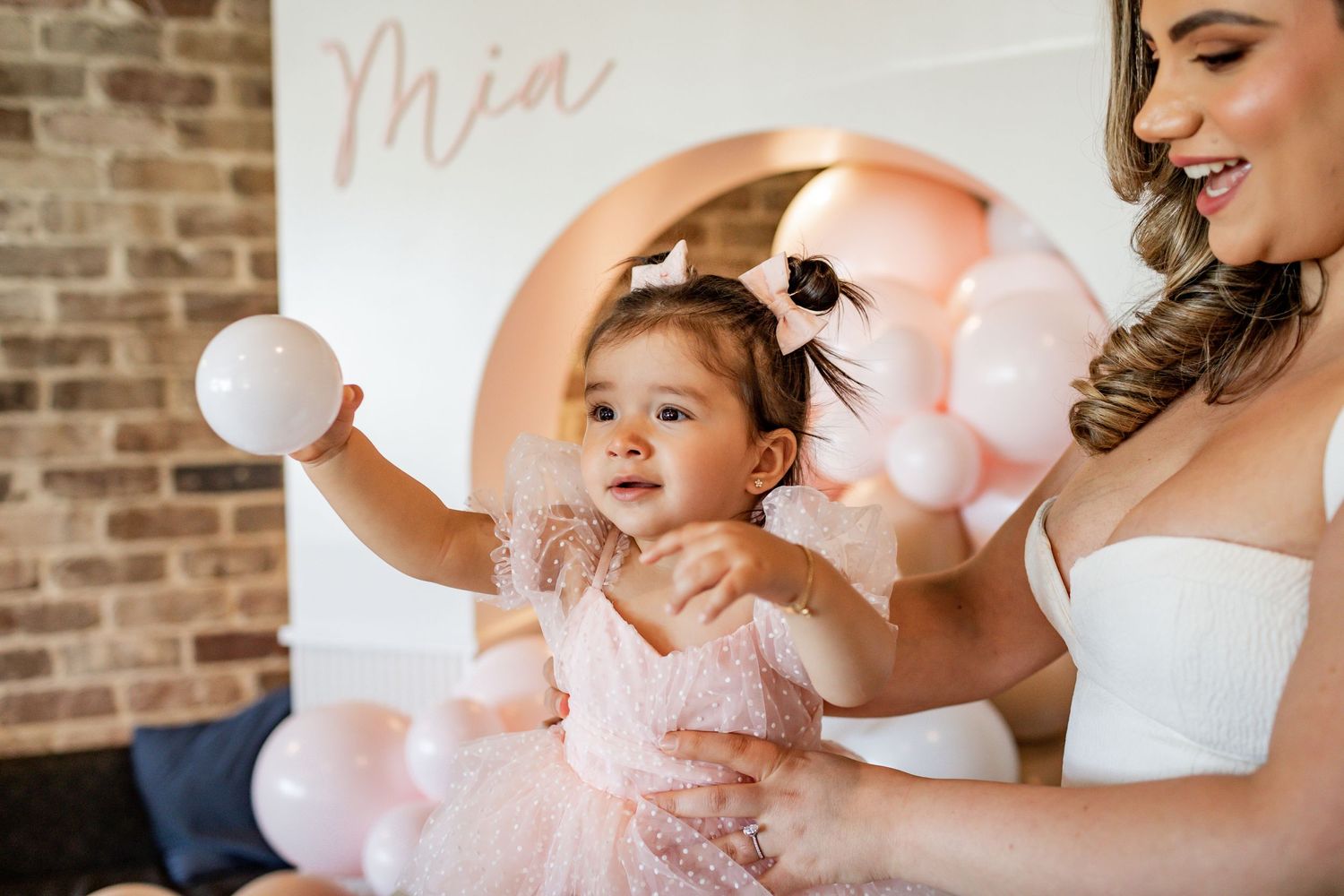 Joyful celebration moment with pink and white balloon decorations against brick wall.