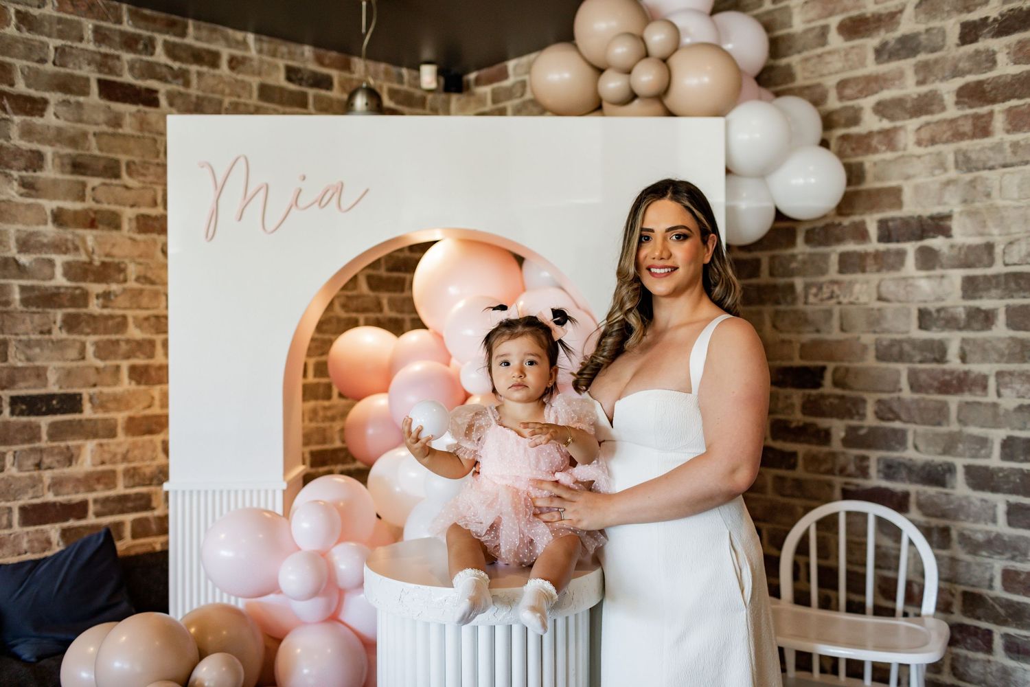 A pink and white balloon decorated party setup with a decorative white panel and column display.