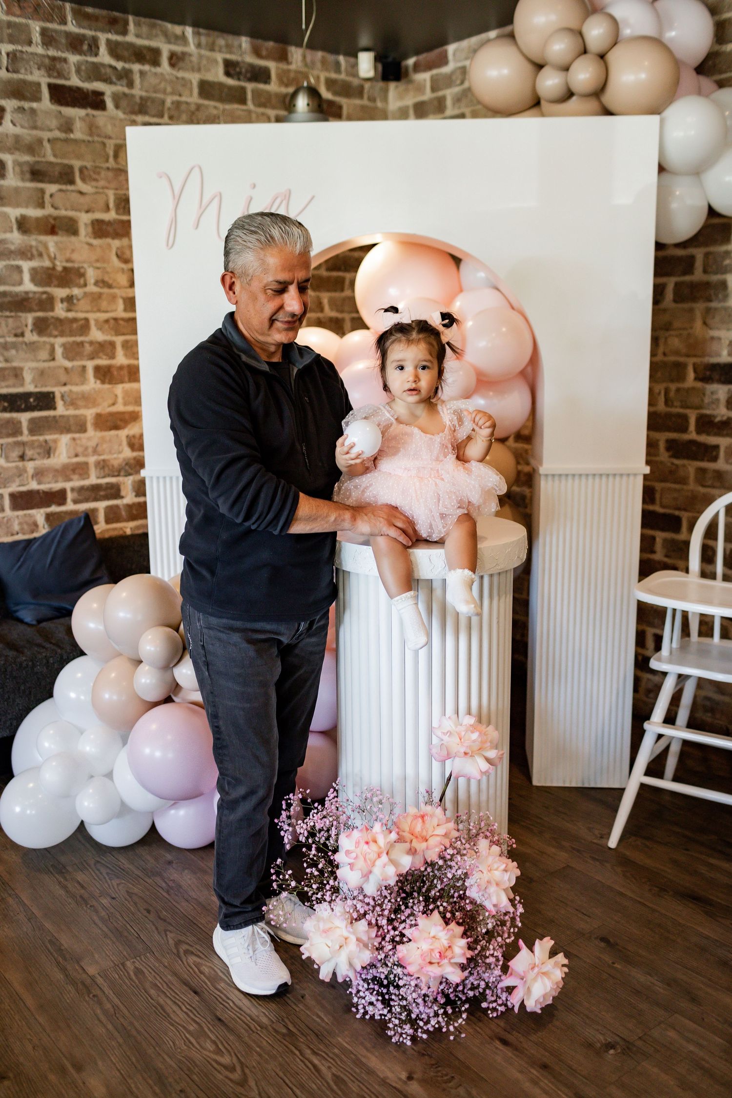 Party scene with decorated white backdrop, pink balloons and floral arrangements.