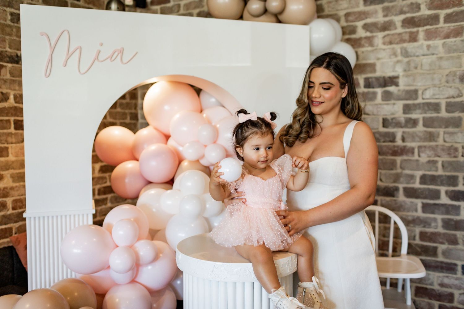 Elegant party setup with pink balloons and 'Mia' text against brick wall backdrop.