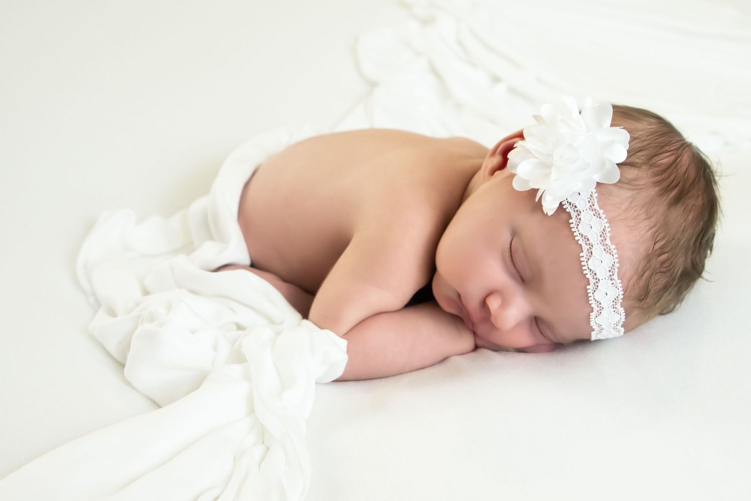 Artistic series of baby sleeping in white lace wrap against light background.