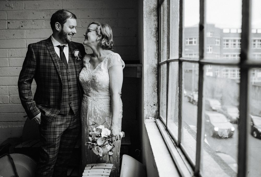 Black and white wedding portrait by large industrial window showing intimate moment.