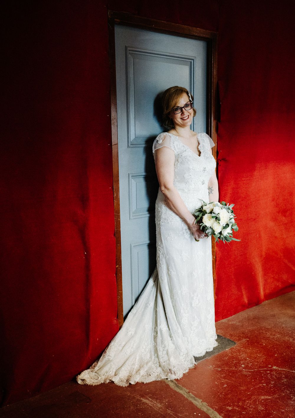 Wedding attire against vibrant red wall and blue door creating dramatic contrast.