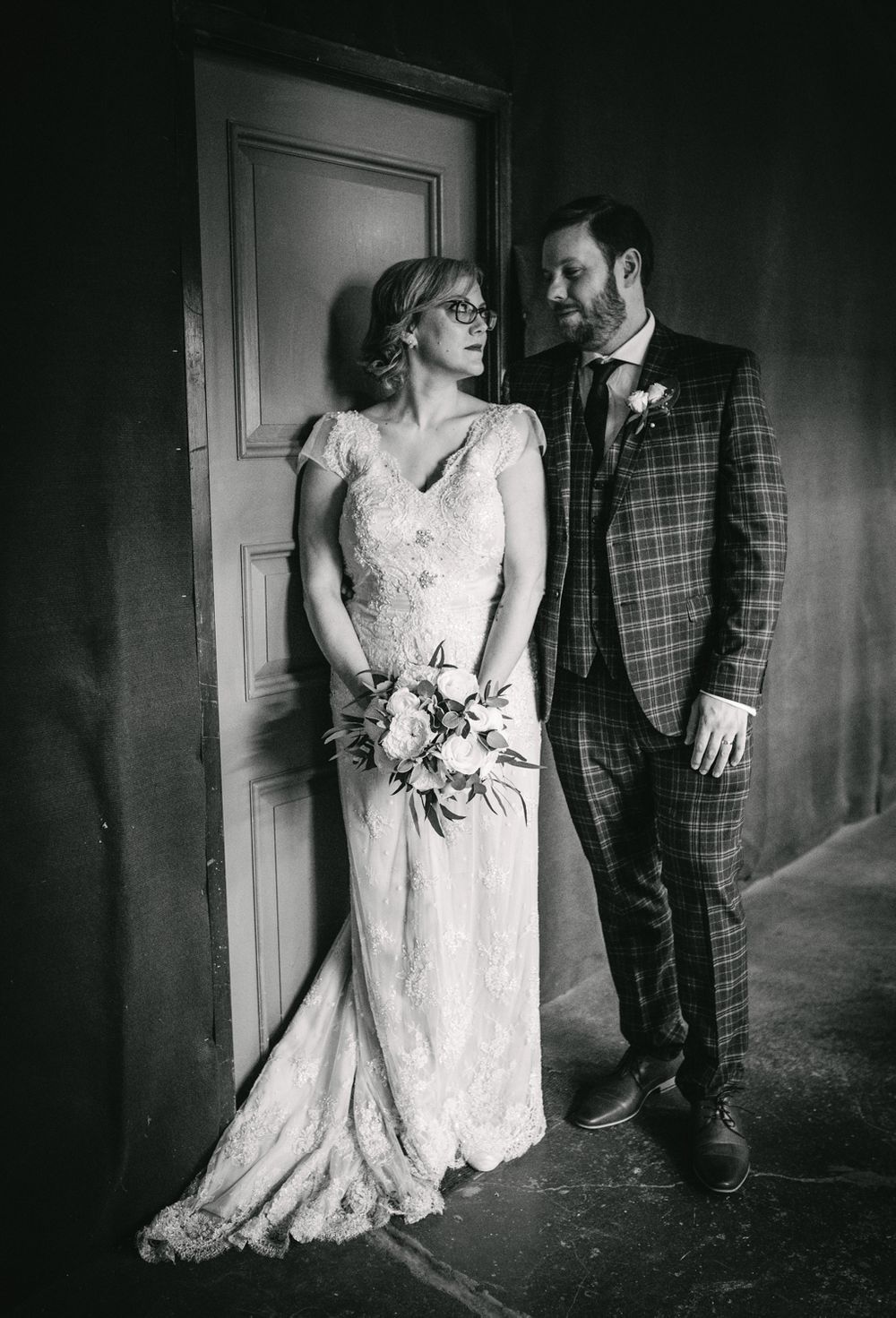 Vintage-style black and white portrait of wedding couple against rustic door.