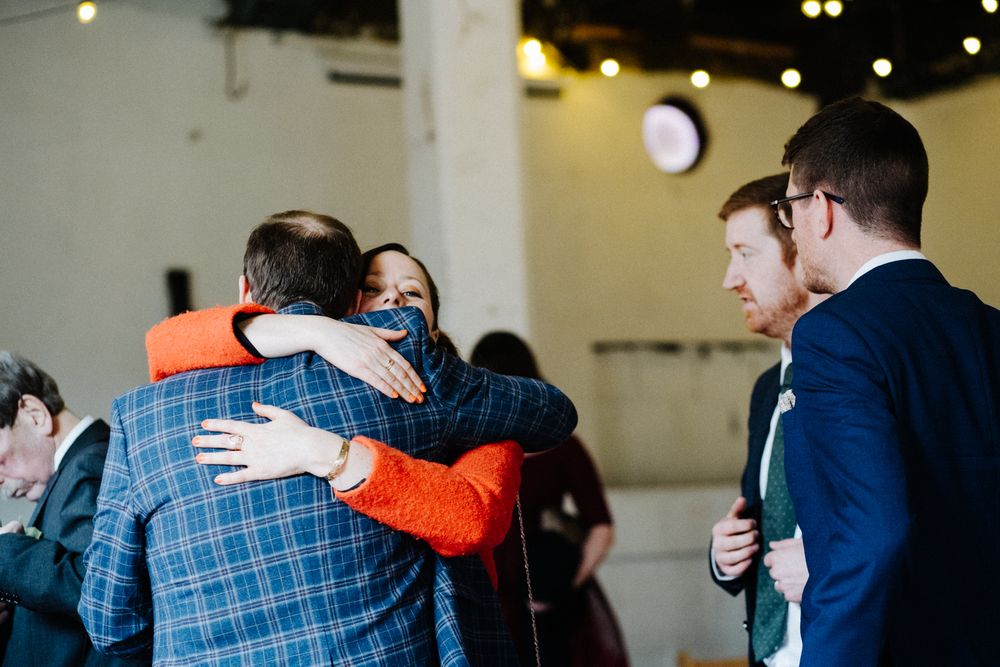Celebratory embrace at indoor gathering with guests in formal attire.