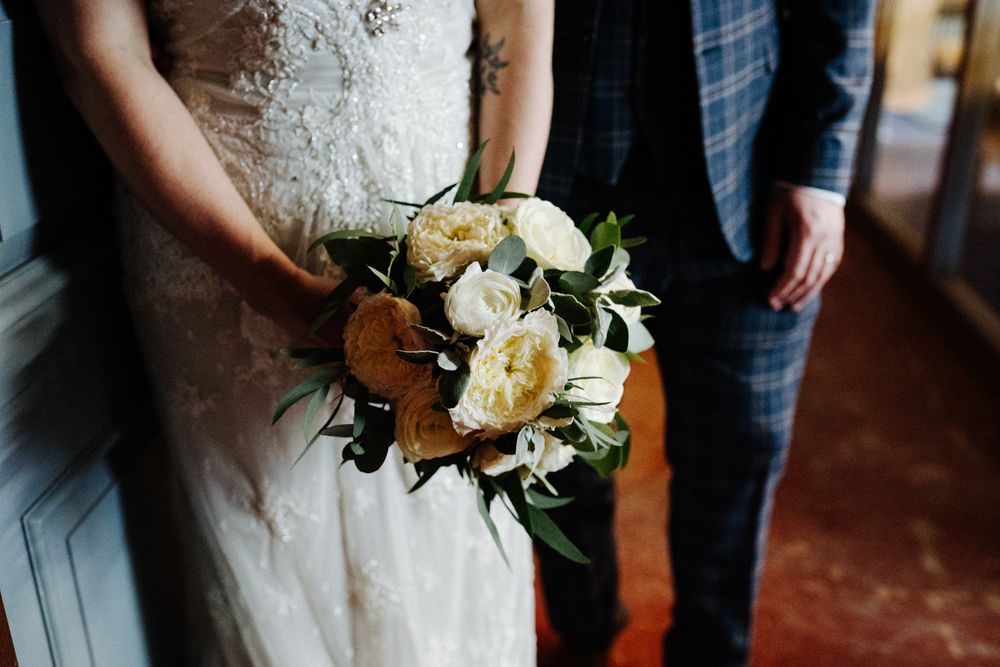 Elegant white rose and greenery wedding bouquet held against lace dress and plaid suit.