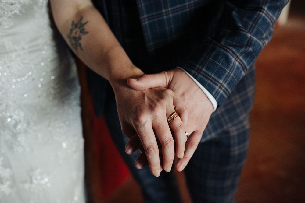 Close-up of newlywed hands with rings and visible tattoo against plaid suit fabric.
