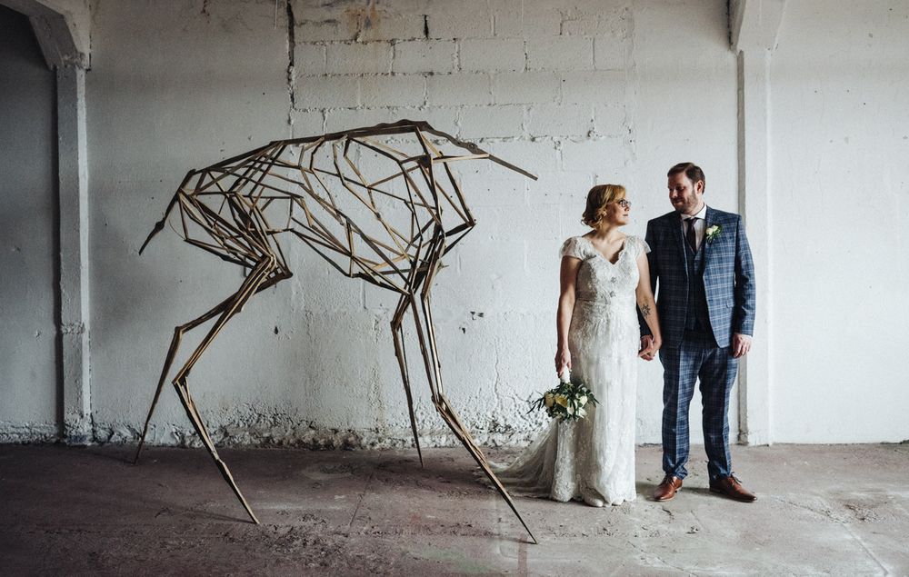 Modern wedding portrait with artistic metal wire sculpture in minimalist industrial space.