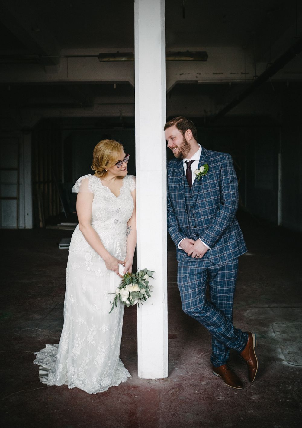 Creative wedding photo with couple on opposite sides of white pillar in industrial setting.