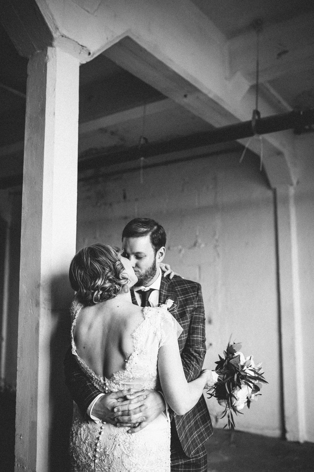 A romantic black and white wedding moment captured as newlyweds embrace by a pillar.