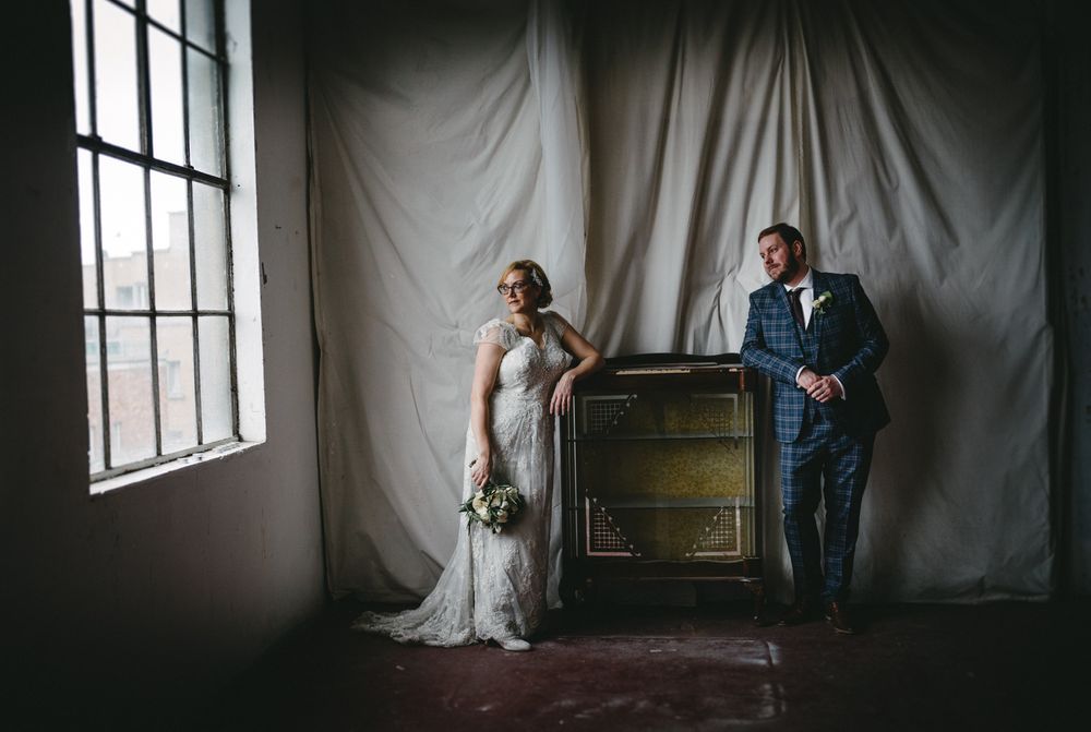 Artistic wedding portrait in moody lighting with vintage piano against white backdrop.