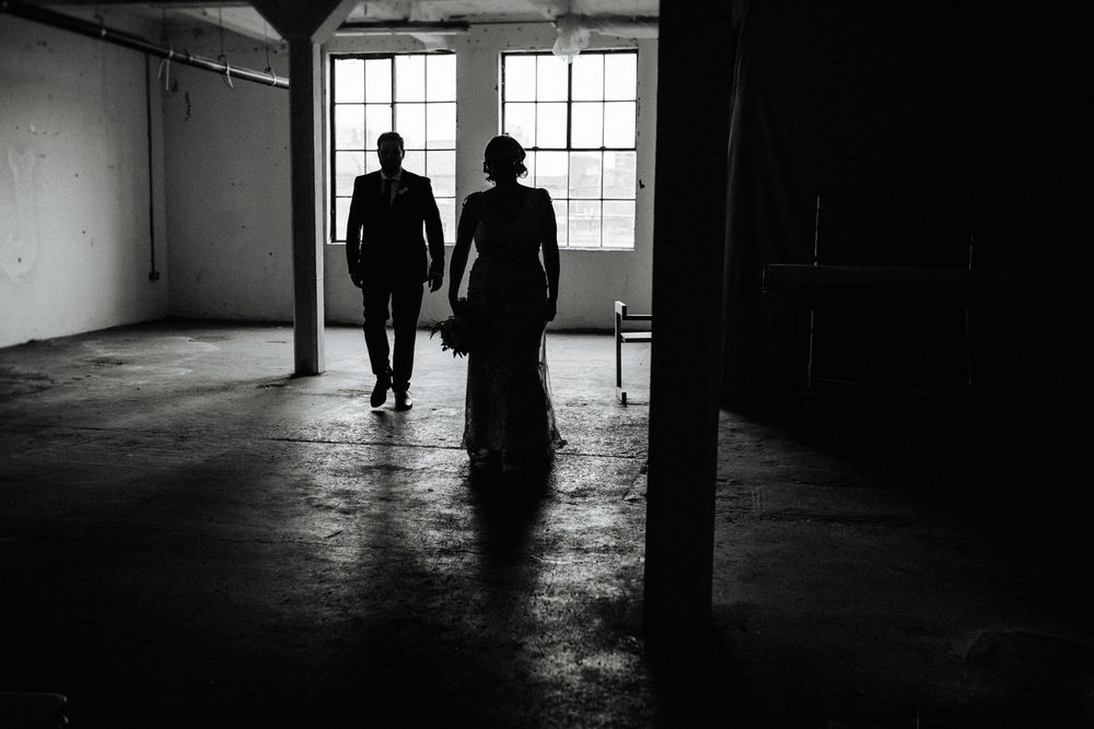 Silhouetted figures walking through an empty industrial space with dramatic window lighting.