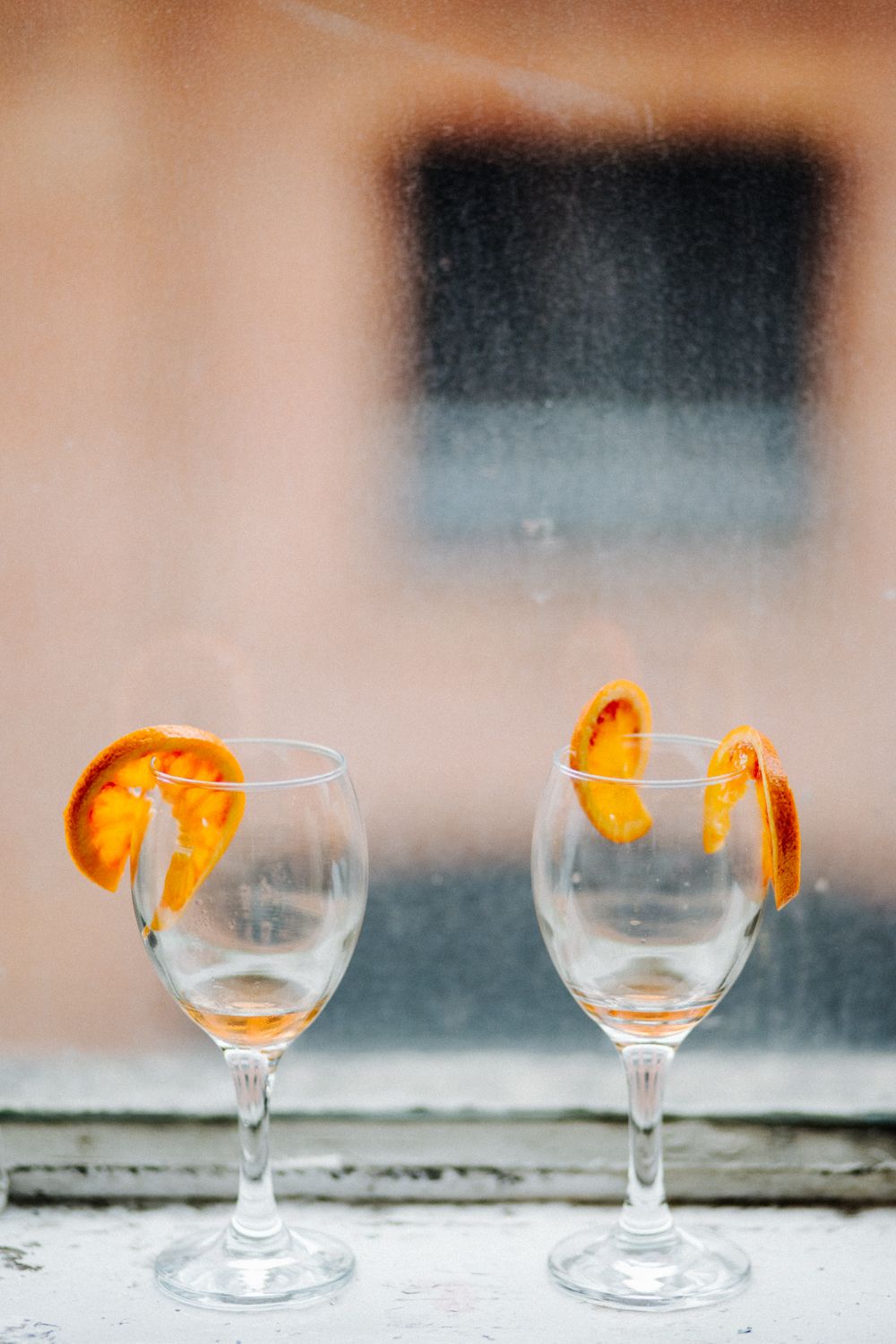 Two empty wine glasses garnished with orange slices sit on a windowsill.