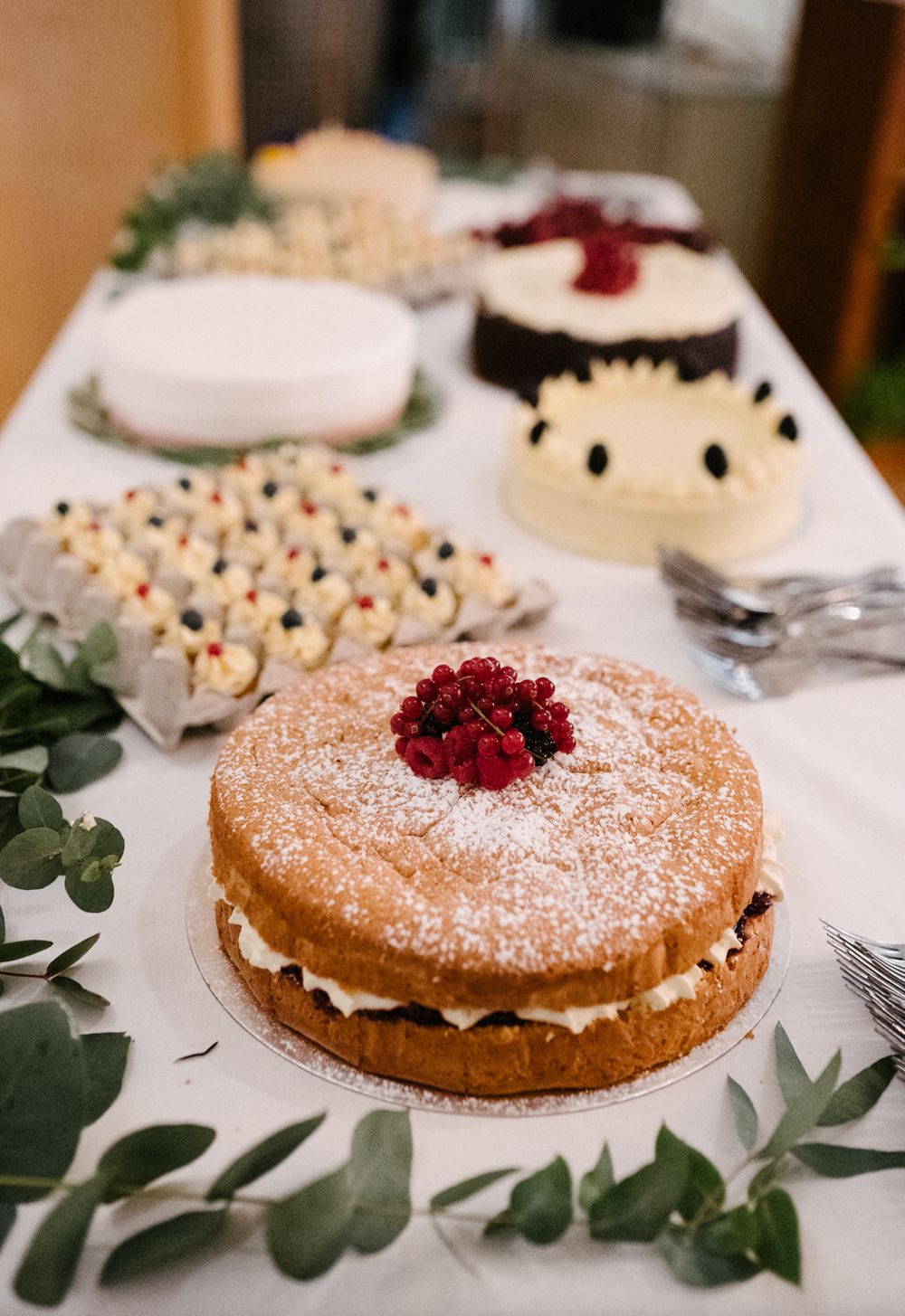 Elegant dessert table with a cream-filled cake topped with raspberries and powdered sugar.