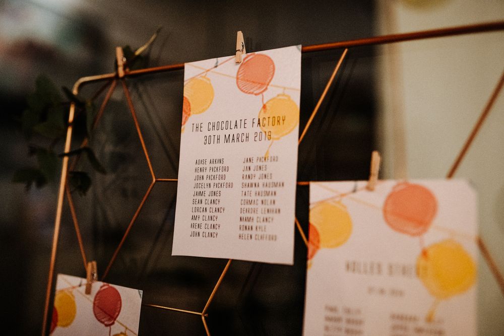 Wedding seating chart cards with orange and yellow citrus designs hanging on copper wire display.