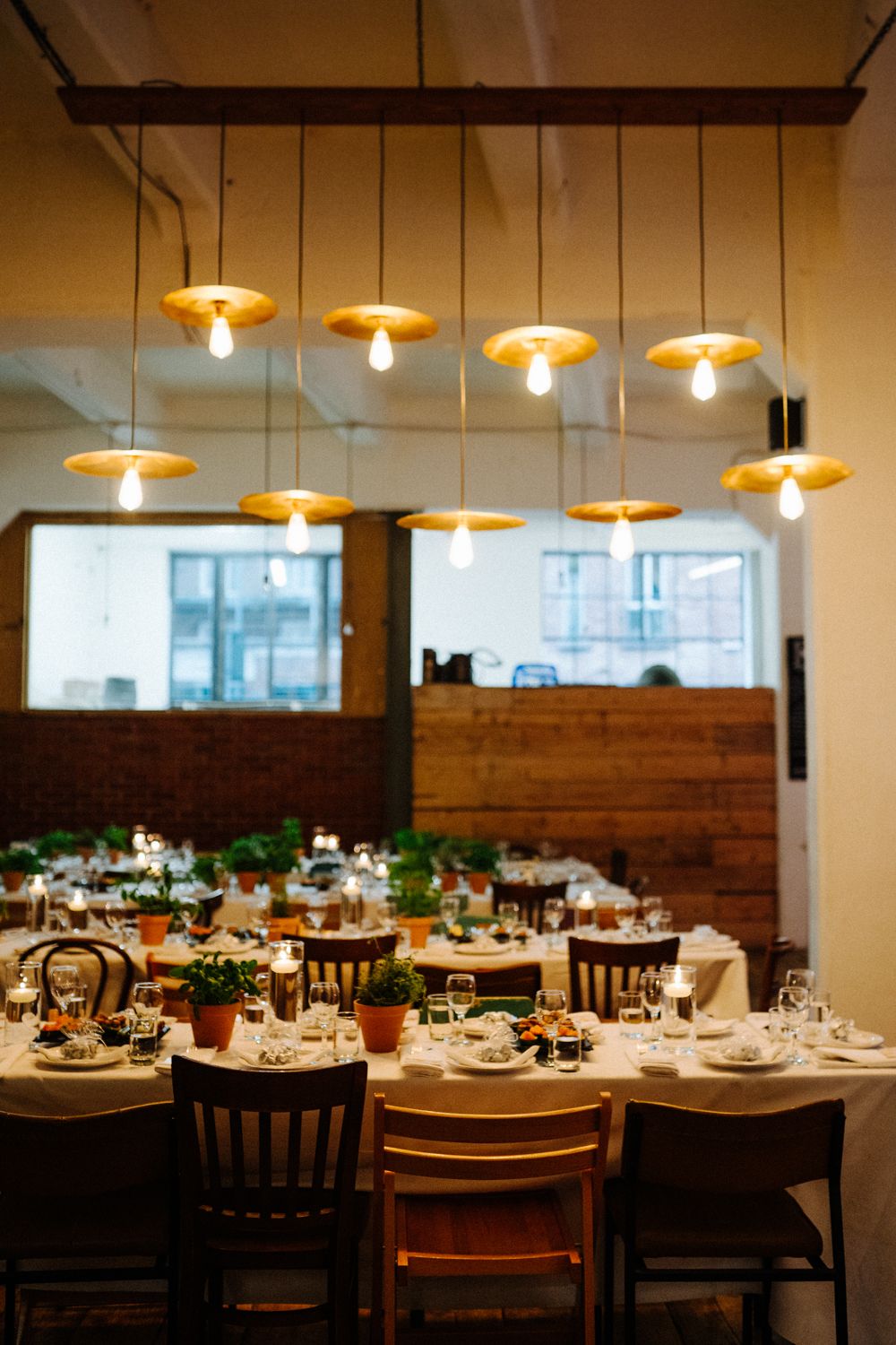 Restaurant dining room with hanging pendant lights and wooden tables set for dinner service.