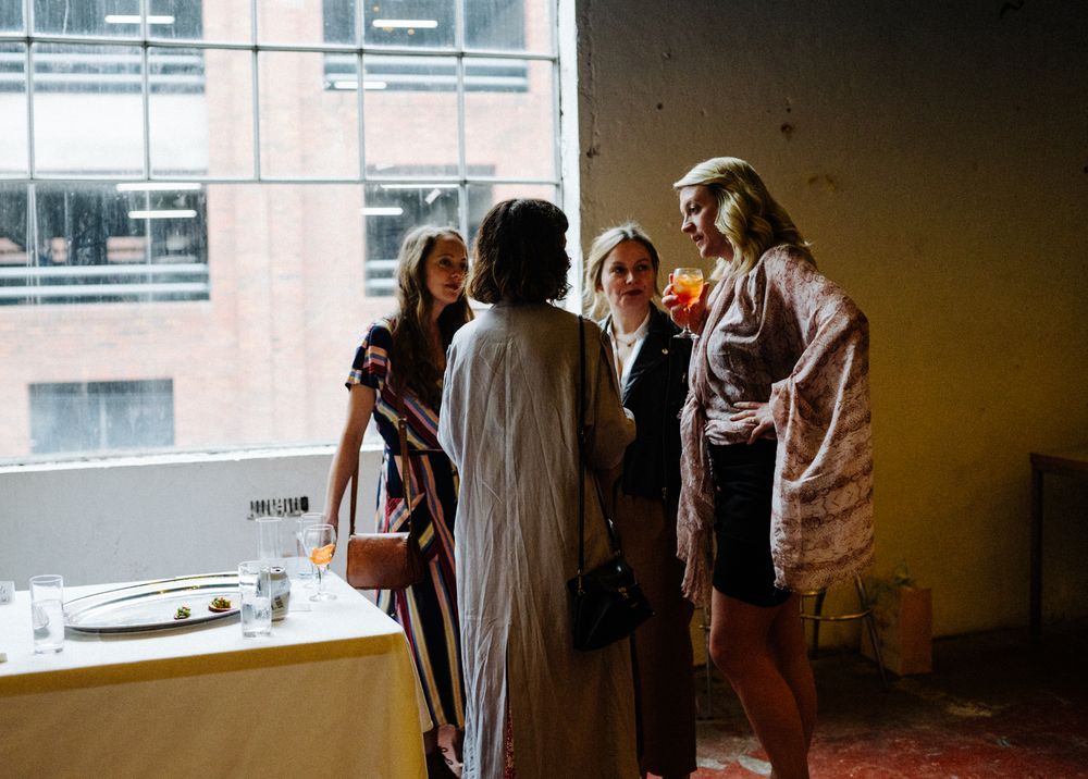 Small group gathered by window in casual conversation at indoor event.