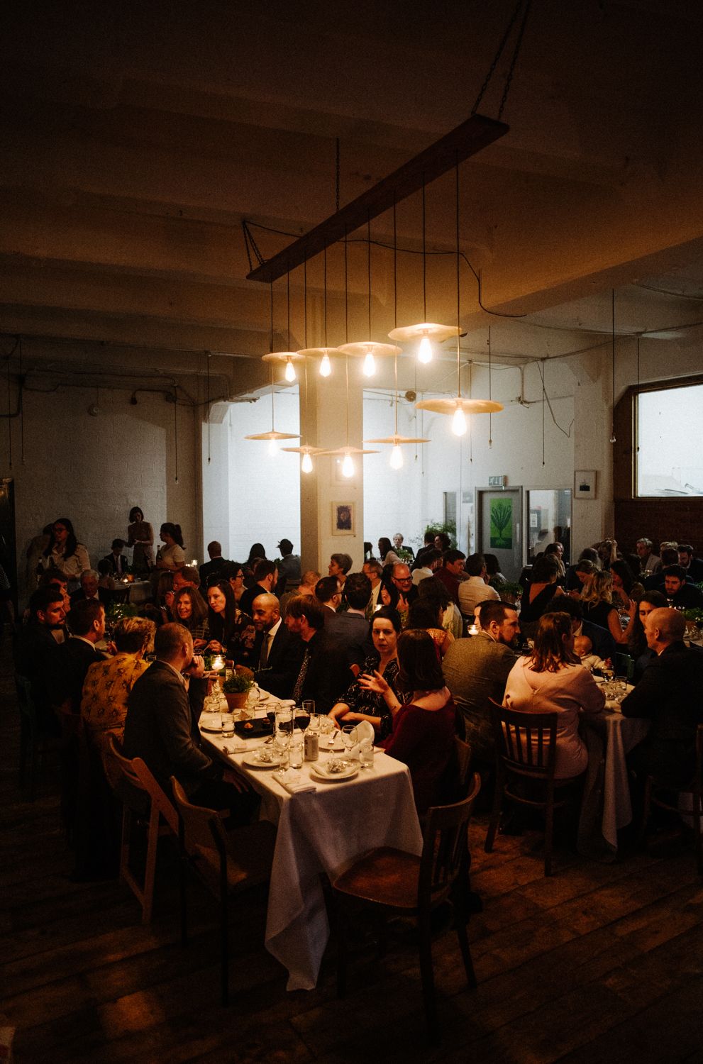 Dimly lit restaurant filled with guests dining at tables under pendant lighting fixtures.
