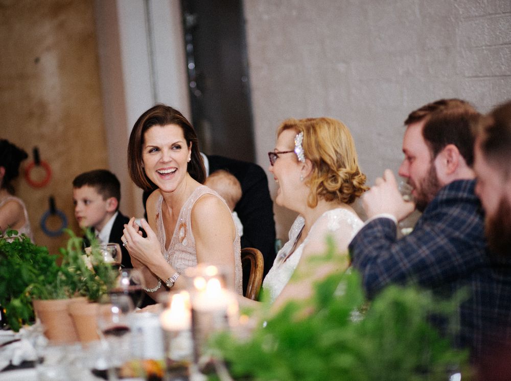Candlelit wedding reception with guests laughing and enjoying dinner conversation.