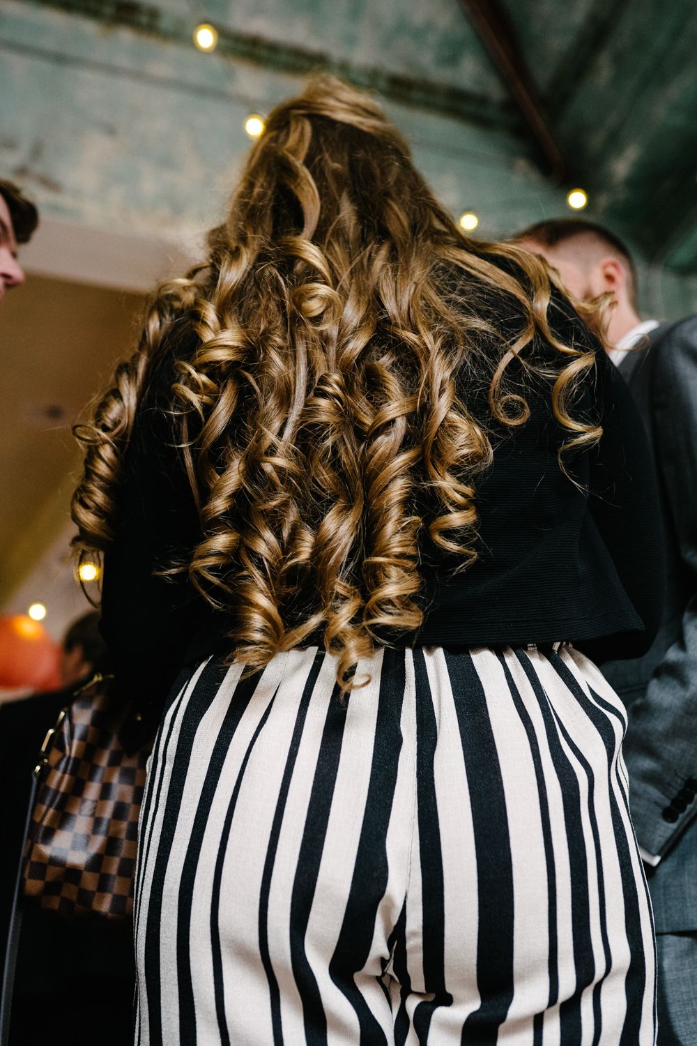 Long curly blonde hair contrasts with a black and white striped dress at a formal event.