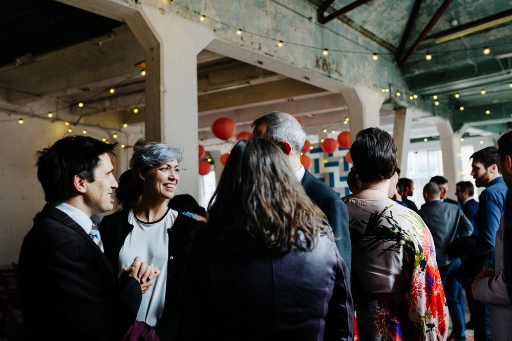 A crowd of people gather at an indoor event space with string lights overhead.