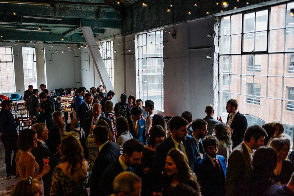 Crowded indoor reception venue with large windows and mingling guests.