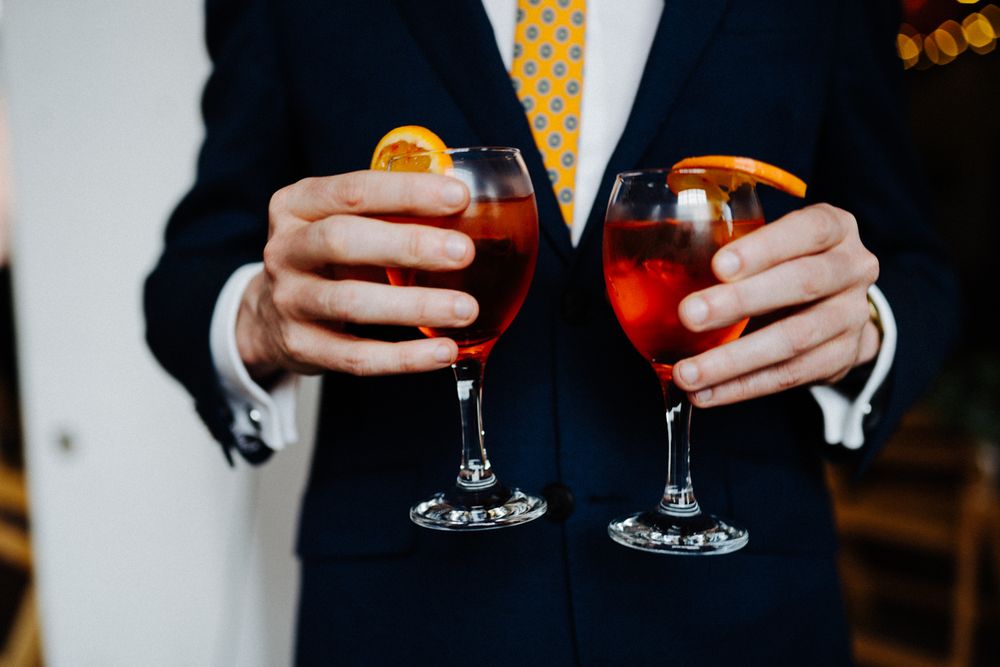 Person in navy suit holding two glasses of red wine.