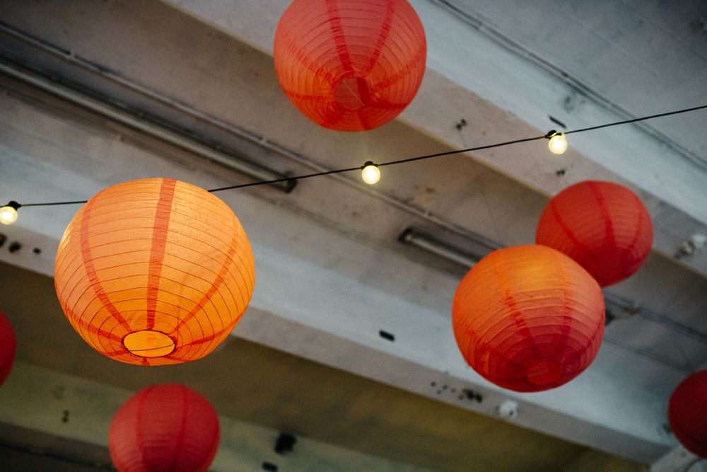 Red and orange paper lanterns hanging from industrial ceiling with exposed pipes.