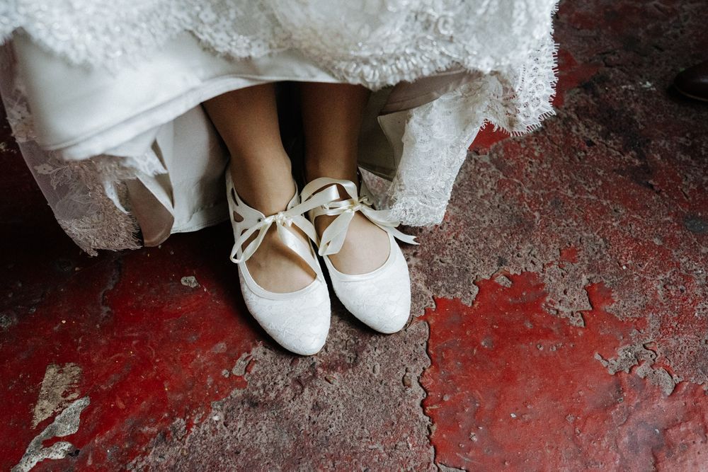 Close-up of bride's white lace-up ballet flats on red textured floor.