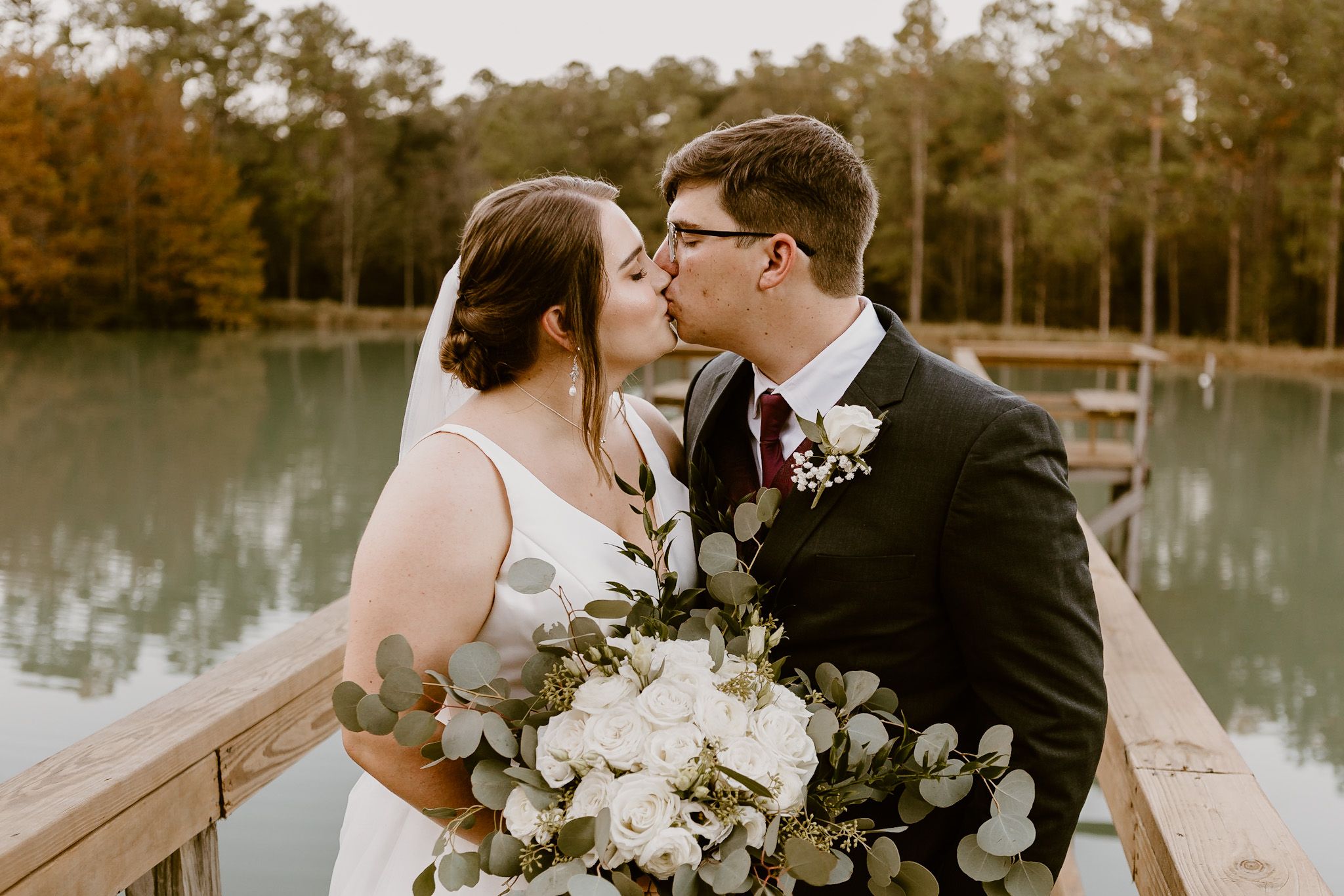 Couple in wedding attire kissing in front of a lake at the Elizabeth wedding venue in Mobile, Alabama.