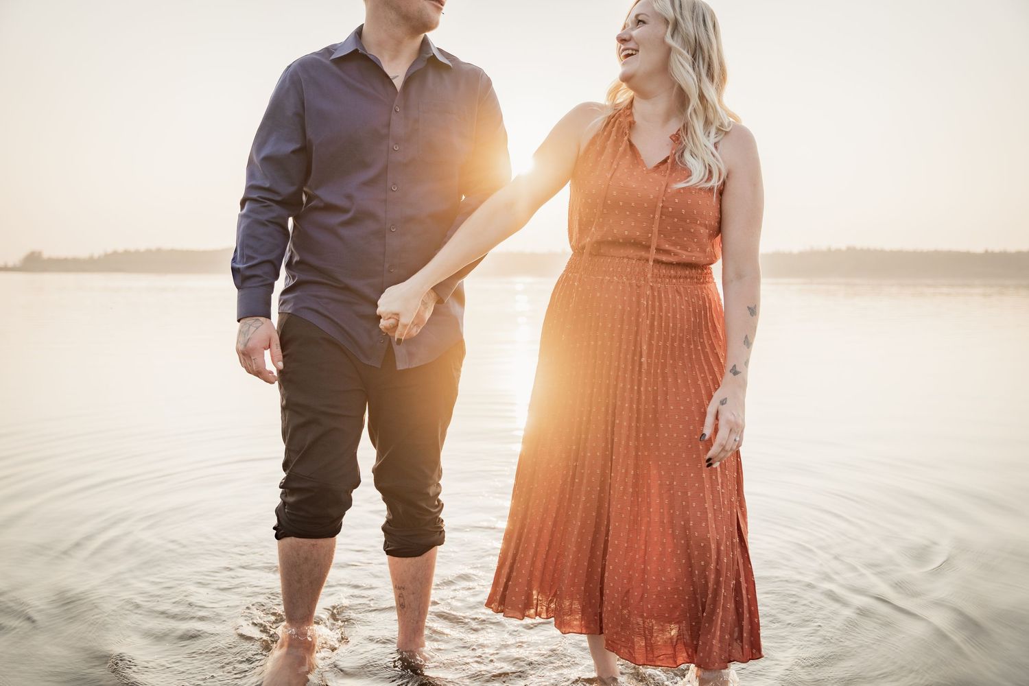 Couple standing at sunset by the water with warm backlight and romantic atmosphere.