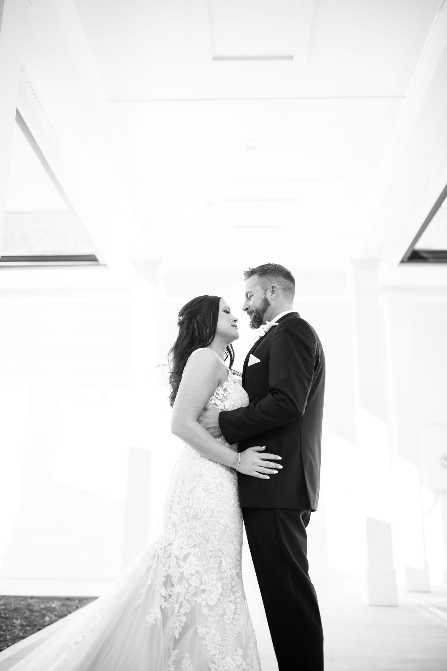 Black and white portrait of couple in wedding attire against white architectural backdrop.