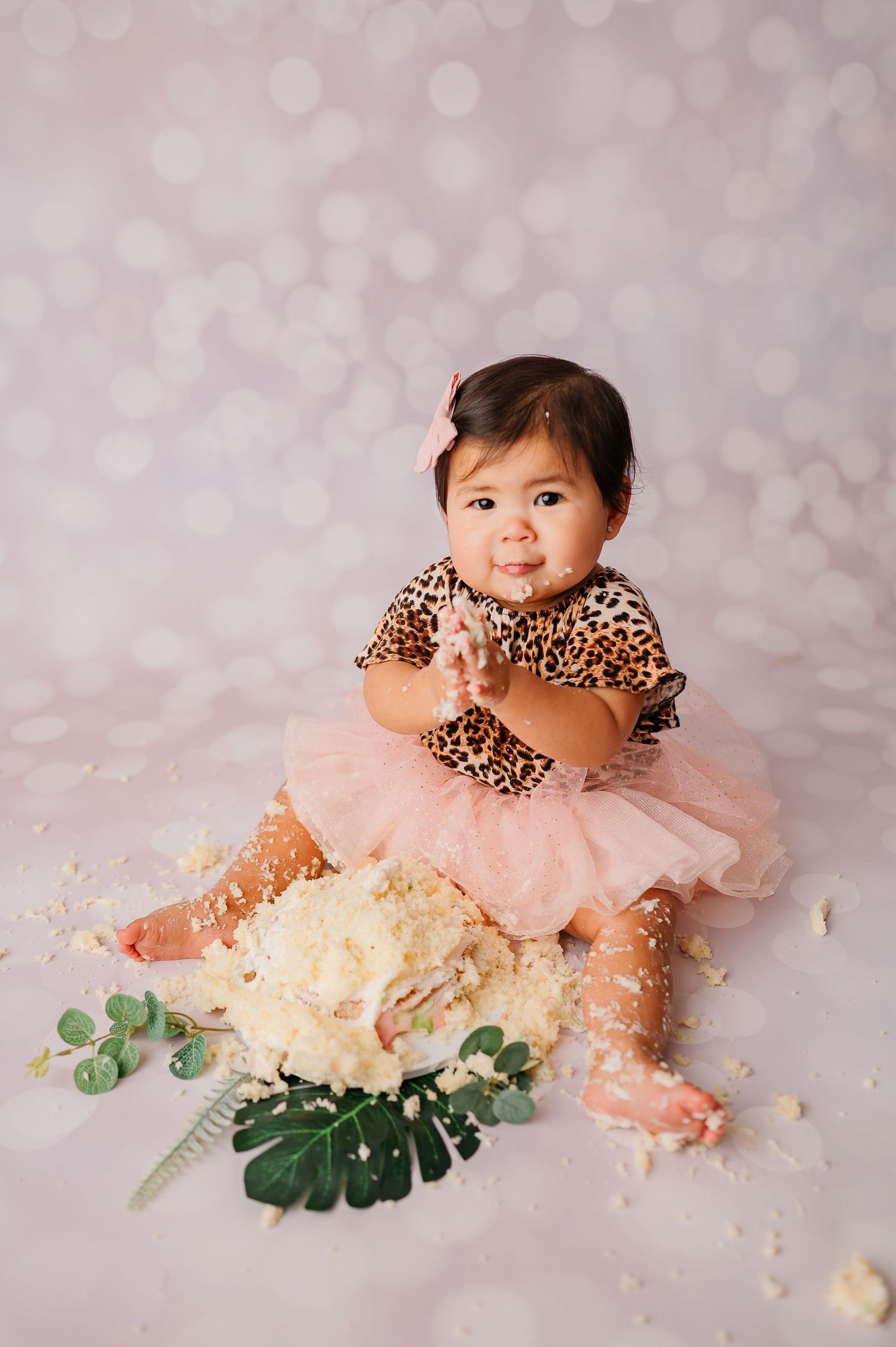 one year old making eye contact with camera with cake all over her hands during her first birthday milestone session