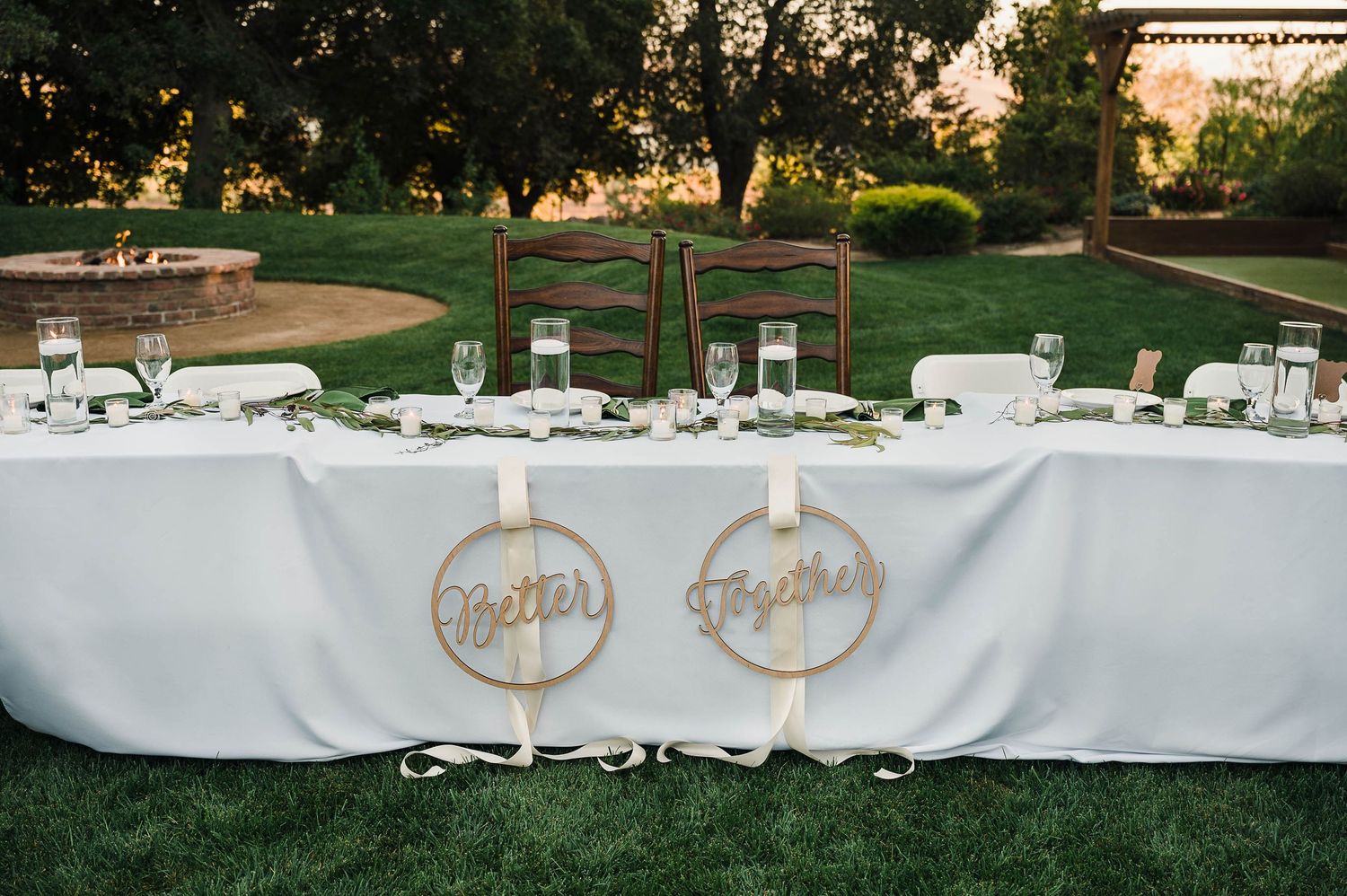 Wedding head table with custom round name signs and white tablecloth against garden backdrop.