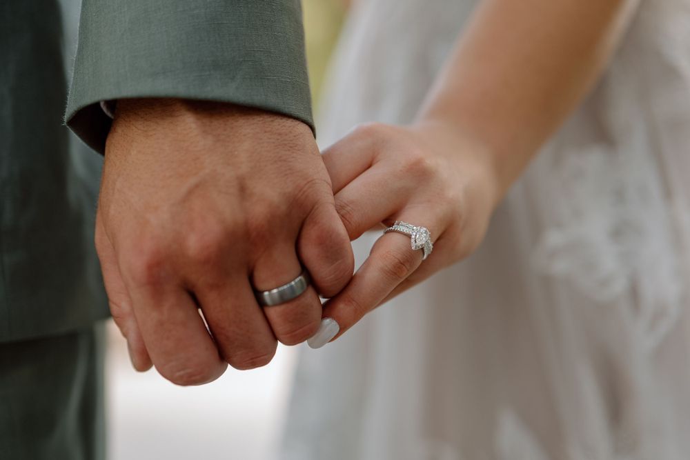 Close up of bride and groom holding hands with wedding bands on