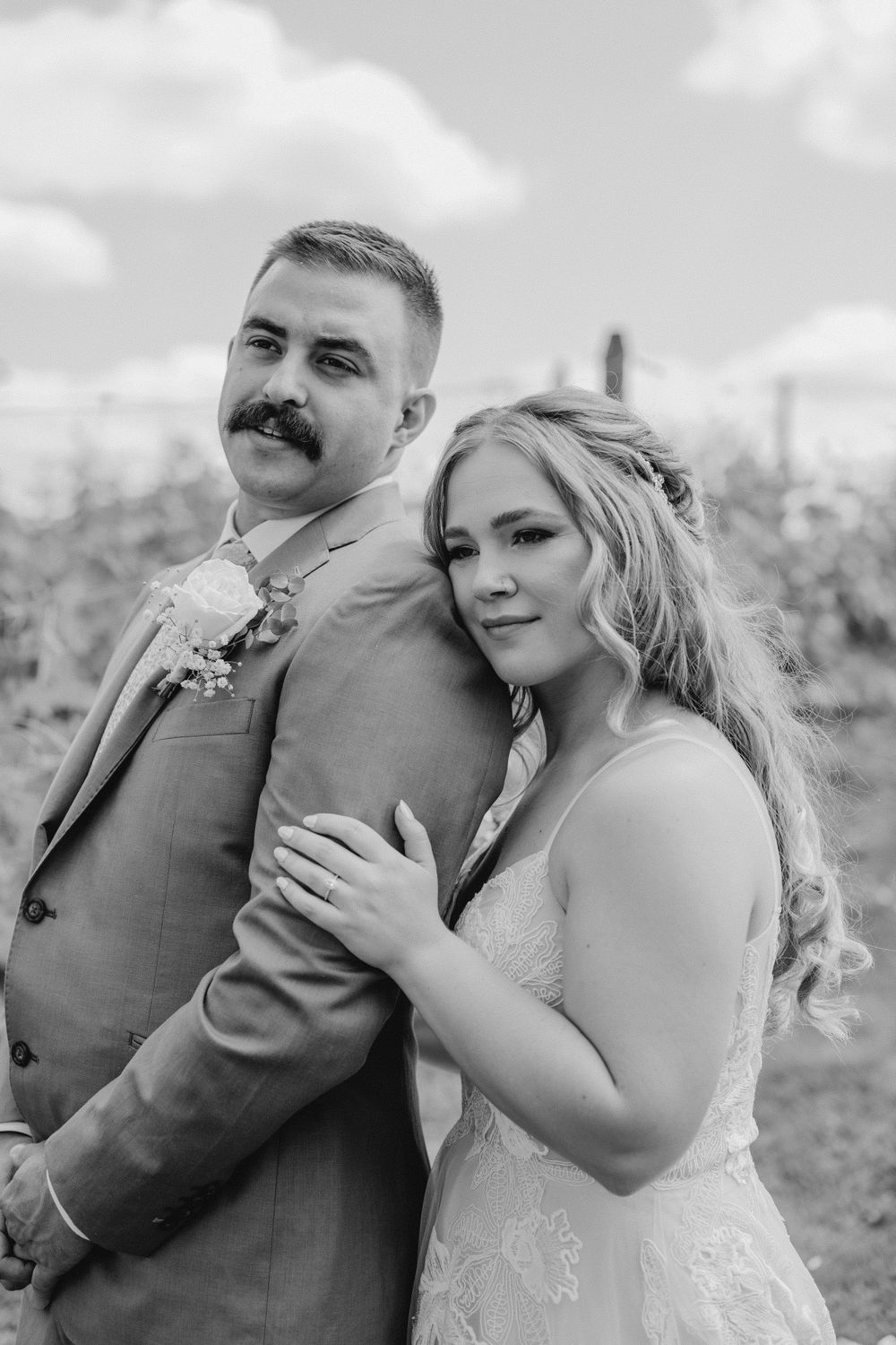 Black and white of bride and groom cuddled in vineyard