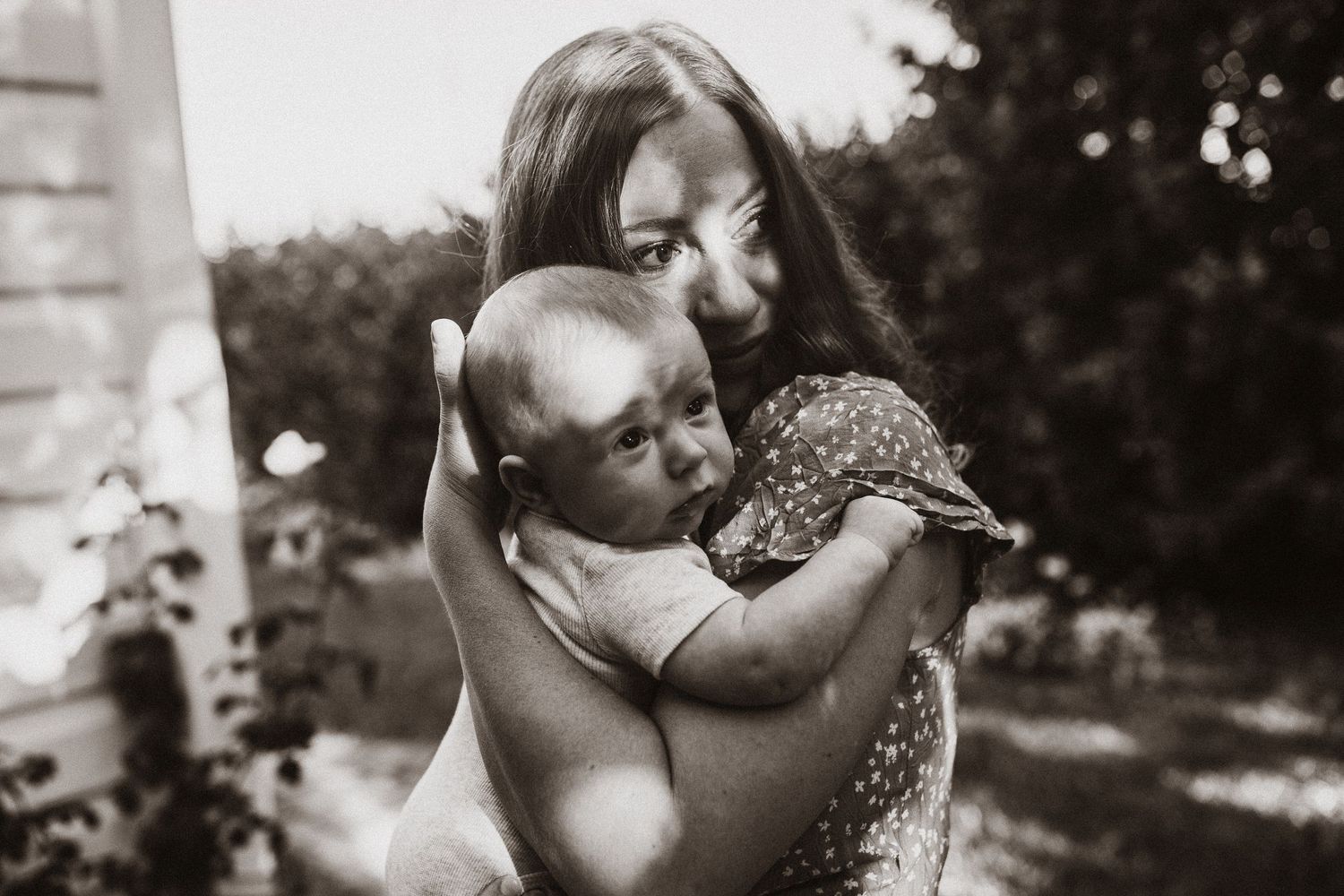 Black and white image of a mother and son cuddling looking off into the distance. Shadows on their faces