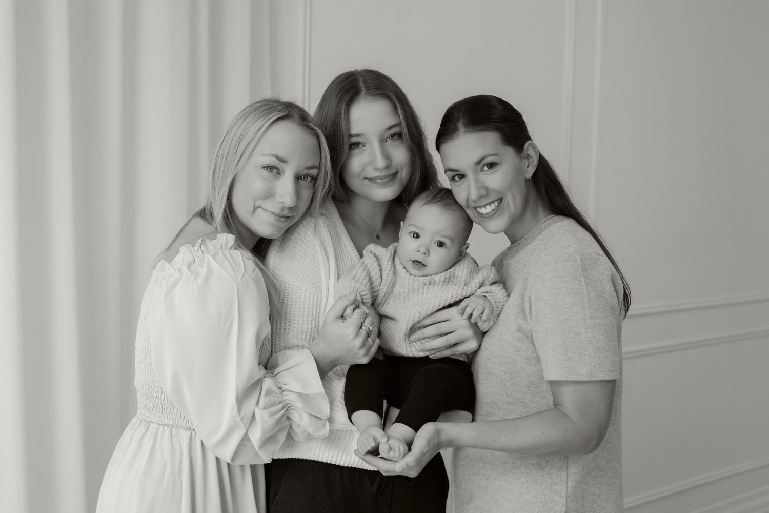 Studio portrait of three women in light clothing holding a baby.