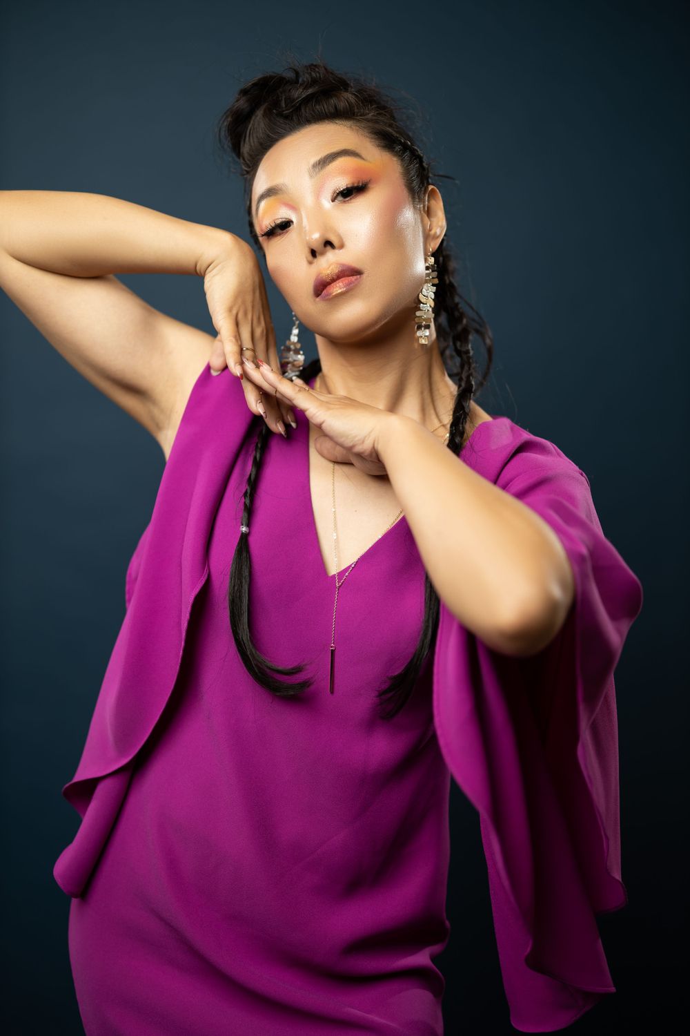 Artistic studio portrait in purple dress with elegant hand pose against dark background.