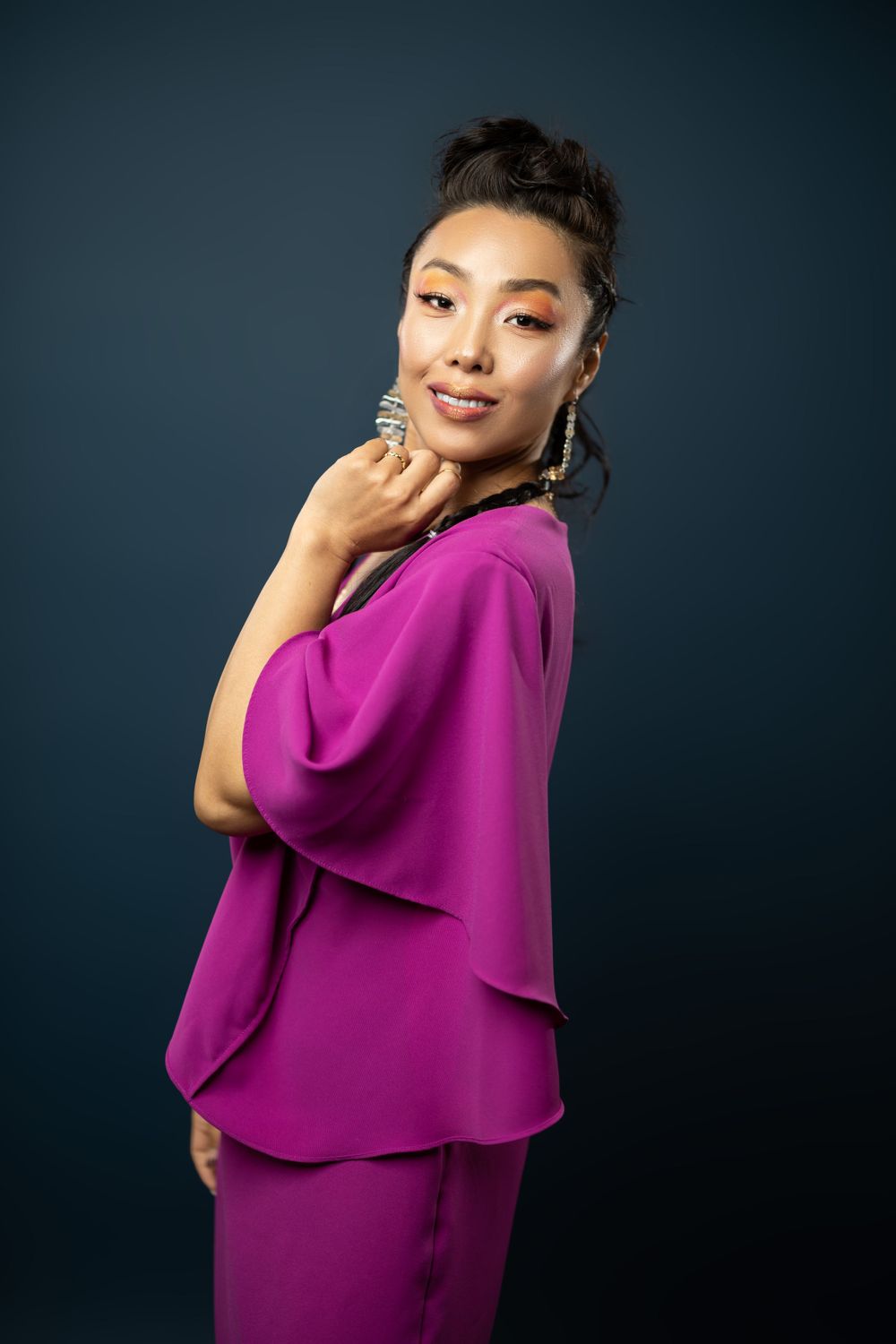 Portrait of an elegant woman in a flowing magenta dress posing against a dark background.