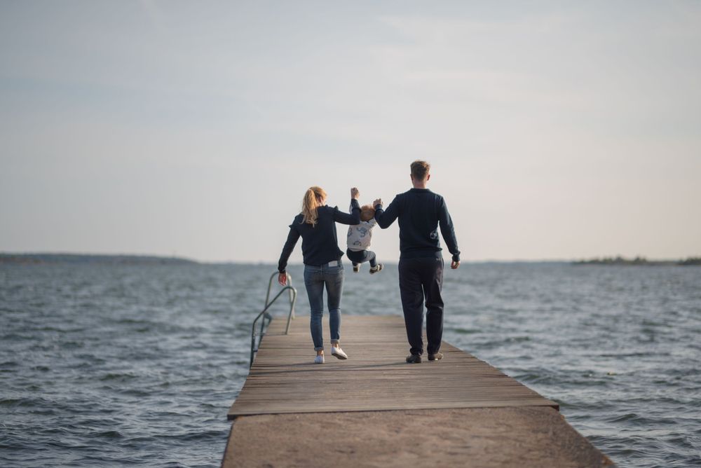 Family holding hands while walking on concrete pier overlooking water.