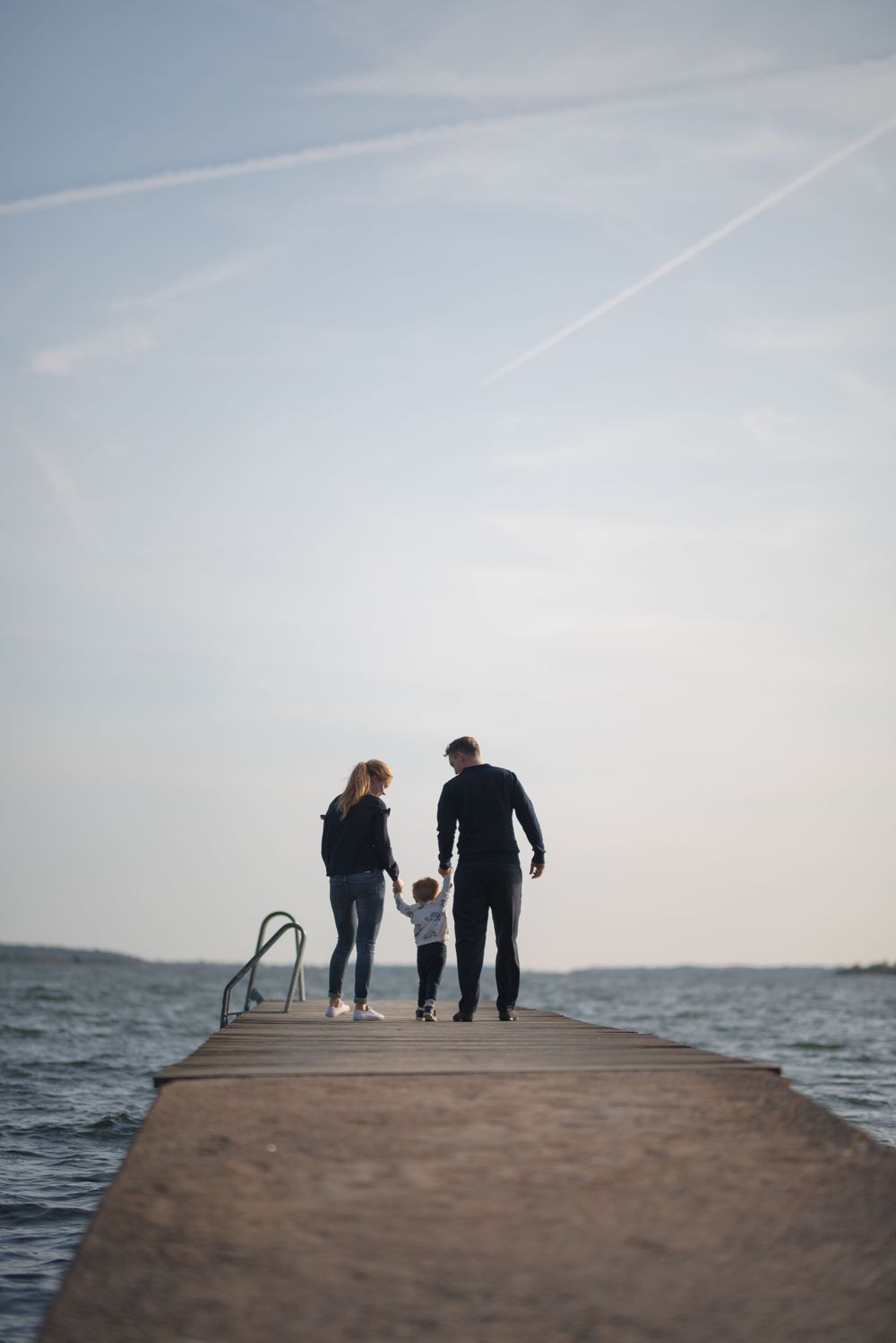 Family silhouettes walking together on wooden pier over water at dusk.