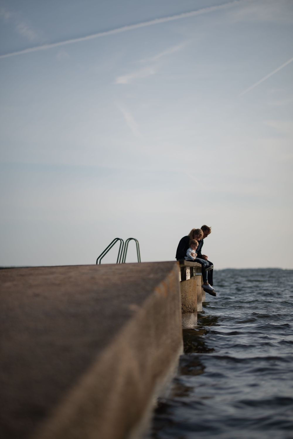 Silhouetted figure sitting alone on edge of concrete pier over water.